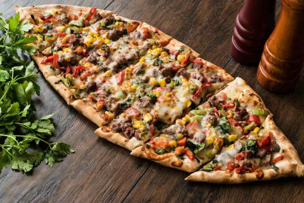 Turkish Pide with meat and vegetables on a wooden surface.